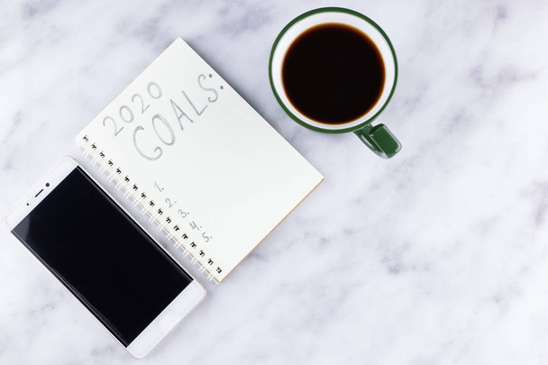 2020 new year goals, plan, action text on notepad on white marble background. 2020 goals on blank note paper with copy space for text. Cup of coffee and smartphone over marble background - Foto, Imagen
