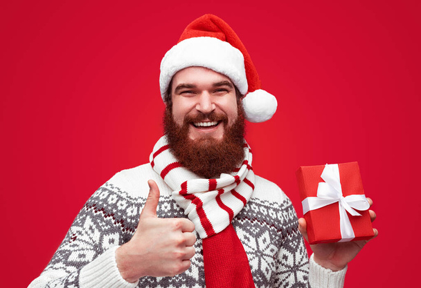 Man with Christmas gift gesturing thumb up - Zdjęcie, obraz