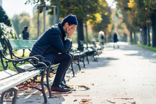 Jeune homme inquiet sur un banc pendant la journée d'automne
 - Photo, image