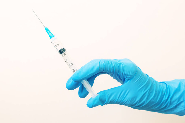 Hand in a blue medical glove with a syringe on a light background. The concept of medicine, vaccination, health. Minimalism, place for text. - Foto, imagen