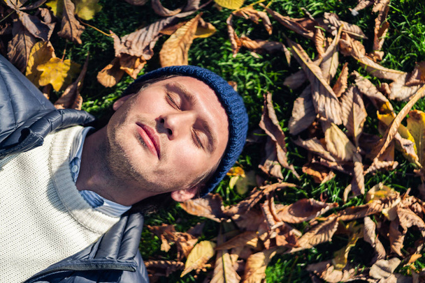 glücklicher junger Mann entspannt sich im Park zwischen Herbstblättern. - Foto, Bild