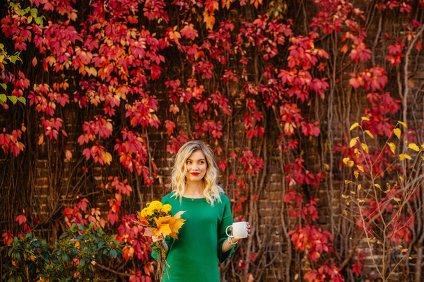 Szőke romantikus fiatal nő tartja bögre forró ital és sárga bouguet őszi virágok - Fotó, kép