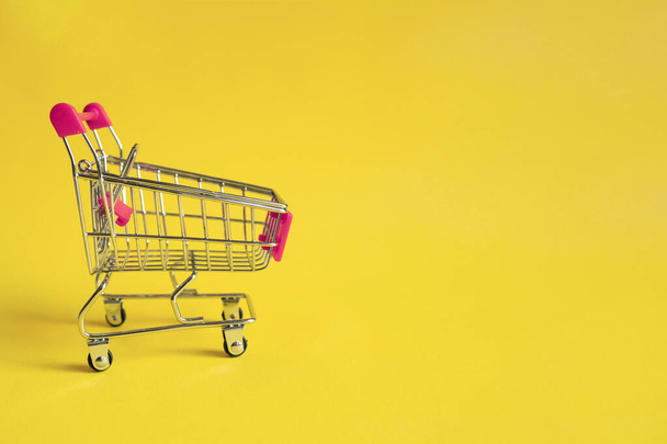 Empty shopping trolley with pink handle on yellow background. Online shopping concept. A form of electronic commerce. - Photo, Image