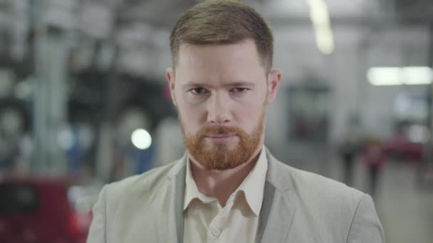 Close-up face of adult Caucasian man with brown eyes and red beard gesturing yes by shaking head, and smiling. Male car dealer posing at the background of showroom. Car dealership, car business. - Záběry, video