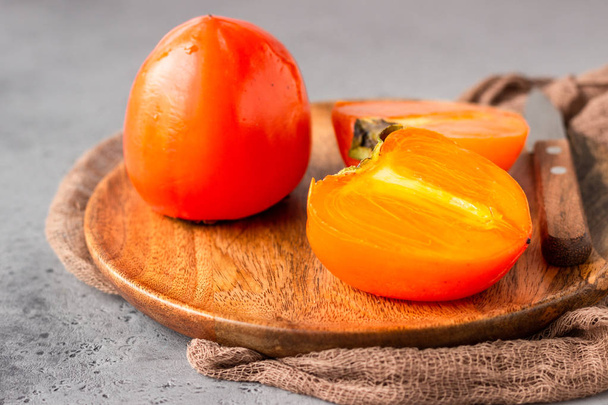 Ripe orange persimmon fruit with knife on a wooden plate. Healthy food. - Fotografie, Obrázek