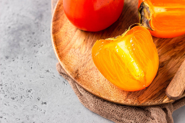 Ripe orange persimmon fruit with knife on a wooden plate. Healthy food. - Foto, afbeelding
