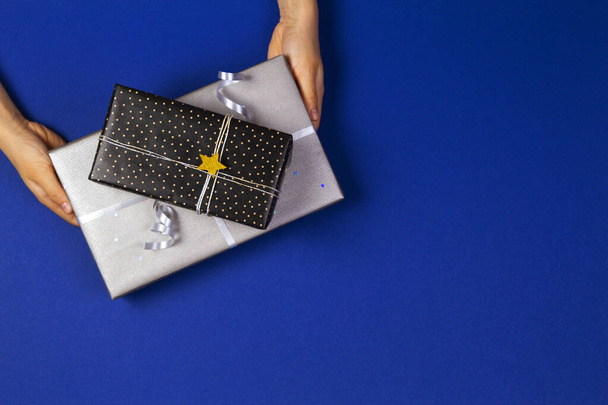 Hände, die Geschenke in Geschenkpapier auf marineblauem Hintergrund verpackt halten. Weihnachten, Neujahr, Urlaubskonzept - Foto, Bild