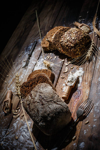 Fragrant and tasty black bread with spices lies next to the spikelets and seeds on a vintage surface - Φωτογραφία, εικόνα