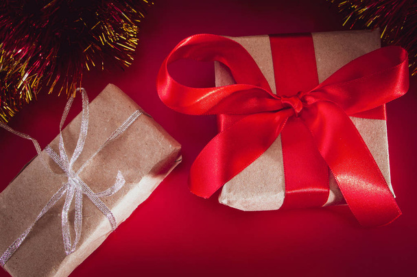 O presente de Ano Novo com uma fita vermelha no papel marrom de ofício. Composição de Natal de cones, ouropel e presentes em um fundo vermelho
. - Foto, Imagem