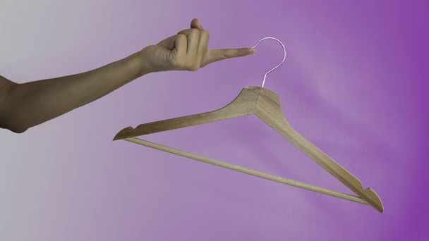 Cintre à vêtements en bois suspendu à un doigt féminin sur un fond violet
. - Photo, image