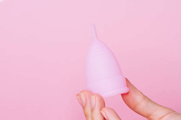 mains de femme tenant réutilisable tasse menstruelle en silicone rose sur fond rose
 - Photo, image