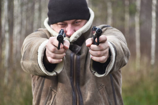 A man with a gun outdoor. The criminal shoots a pistol. Bandit on road - Φωτογραφία, εικόνα