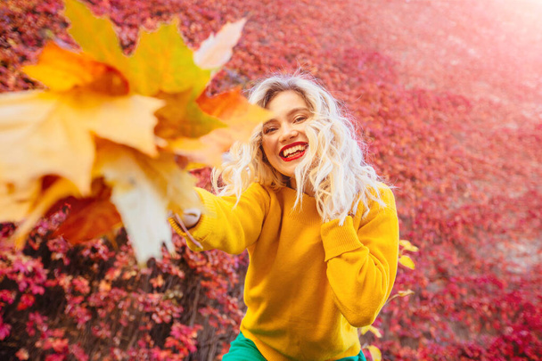 Πορτρέτο της χαρούμενης νεαρής γυναίκας με τα φύλλα του φθινοπώρου μπροστά από το φύλλωμα κάνοντας selfie - Φωτογραφία, εικόνα