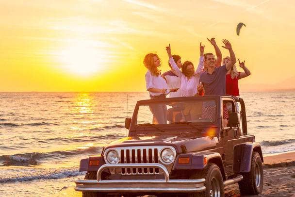 Young group having fun on the beach drink beer and dancing in a convertible car - 写真・画像