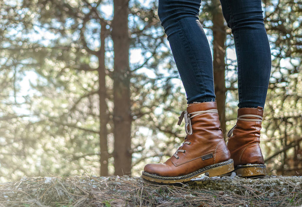 Vrouwelijke poten met leren laarzen van dichtbij te zien in het bos, niet gerichte bomen op de achtergrond. Wandeltoerisme concept. Bos in de bergen.  - Foto, afbeelding