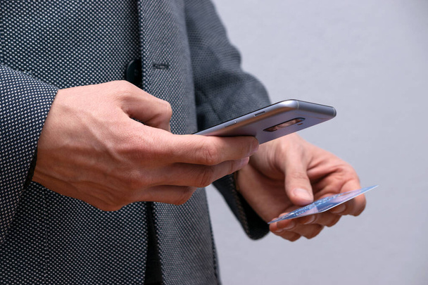 Vista cercana del hombre en traje de compras en línea usando teléfono inteligente y tarjeta de crédito
 - Foto, Imagen