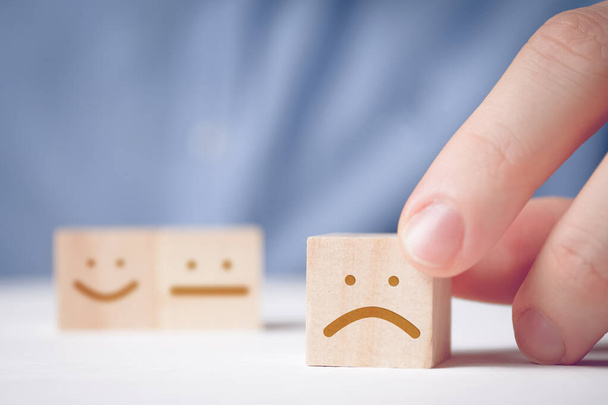 A man holds a wooden cube with a displeased face on a neutral and positive background. Concept for evaluating an action or resource. - Photo, Image