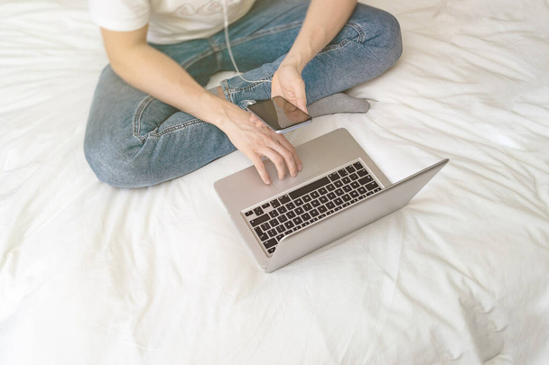Young man caucasian sitting on the bed and working in laptop. Work from home and study at home concept. - 写真・画像