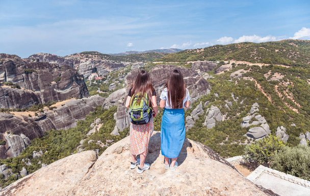 Back view of two young caucasian women tourists looking at view of scenic mountains and rock formations of Meteora Monasteries, Greece. Twin sisters traveling with backpack. - Fotó, kép
