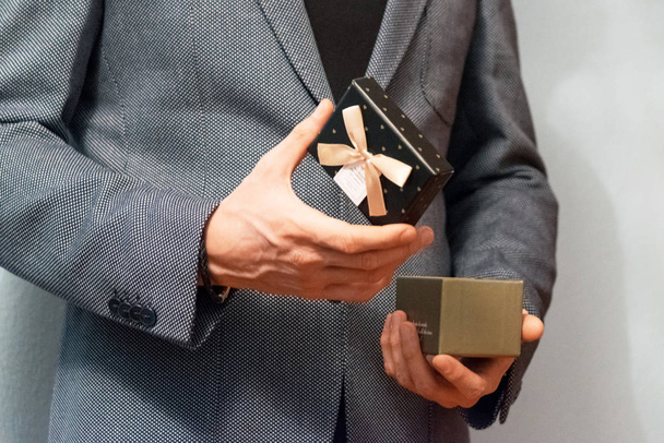 Közelkép egy szürke öltönyös férfiról, amint kinyitja az ajándékdobozt.  - Fotó, kép
