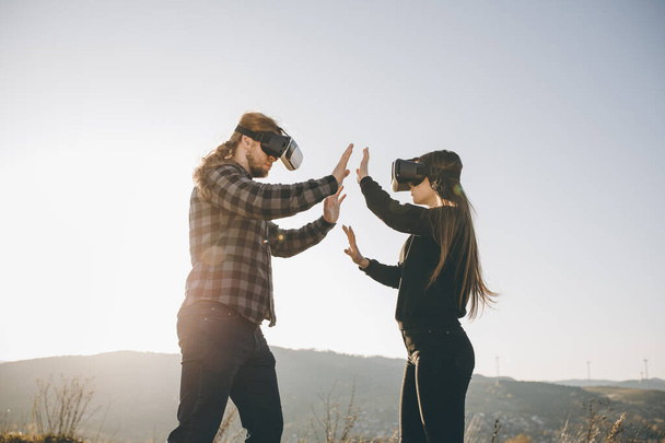 Couple using VR device which are fun virtual computer or video games. Two people uses VR helmet with futuristic visual interface and touches droids hand - Fotoğraf, Görsel