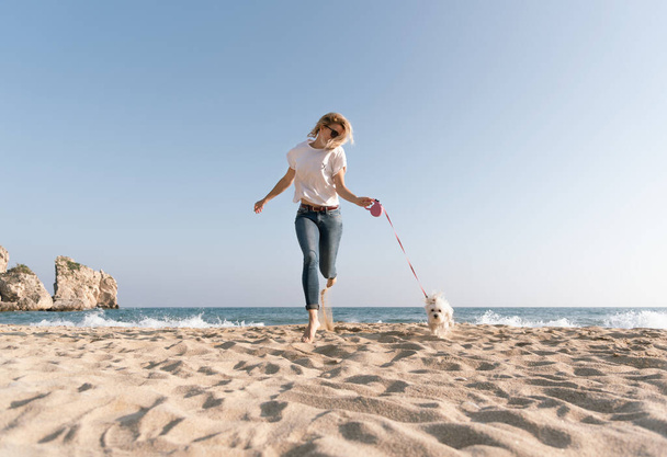Young blonde woman having fun walking with dog by the beach - Foto, Imagem
