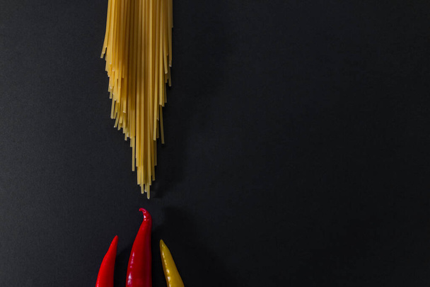 Raw spaghetti and fresh orange red yellow peppers on black surface. Flat lay view. Copy space. Cooking concept. - Fotó, kép