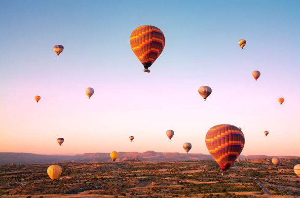 Top view to colorful hot air balloons flying over valleys and fields during sunrise. Turkey, Cappadocia. - Foto, immagini