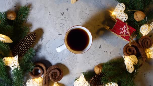 Filiżanka czarnej herbaty lub kawy na stole noworocznym, który jest pobierany przez męskie ręce. Ozdoby świąteczne i noworoczne na stole, gałązki sosny i świerku, szyszki, orzechy, girlandy. Powyżej widoku. - Materiał filmowy, wideo