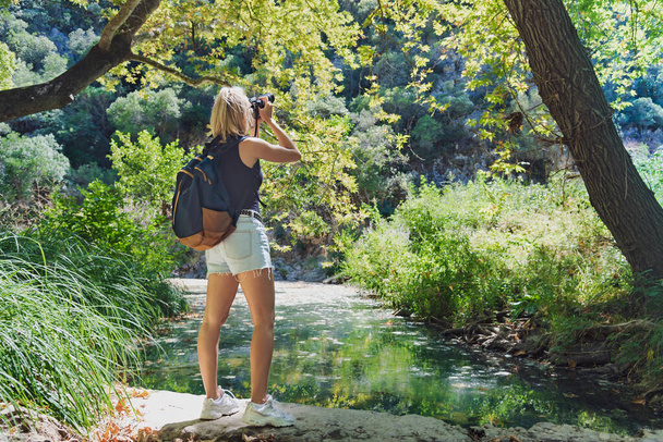 Blonde woman backpacker making photo walking in green forest - Fotó, kép