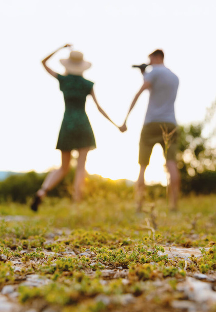 Unfocused silhouettes of man and woman having fun and taking pictures outdoors at sunset. - 写真・画像