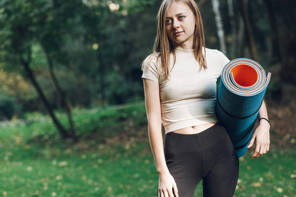 Portrait of young woman with yoga mat in city park. Fitness concept - Photo, image
