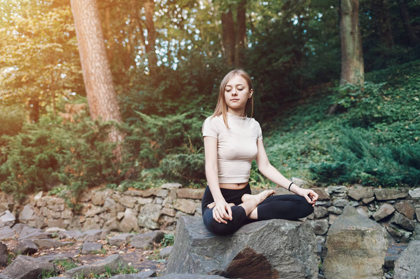 Mulher de ioga sentada em uma pedra na posição de lótus. Conceito de ioga
 - Foto, Imagem