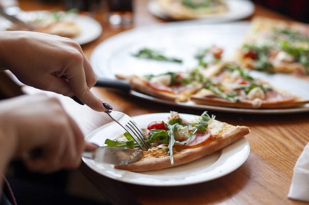 La pizza italiana se come con un tenedor y un cuchillo, una chica corta un pedazo de pizza en un plato
 - Foto, Imagen