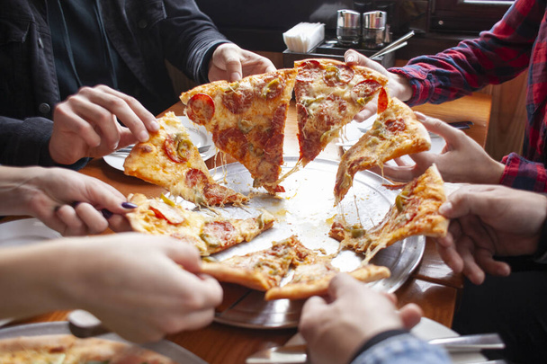 Bir grup öğrenci İtalyan pizzası yer, eller bir restoranda pizza yer. - Fotoğraf, Görsel