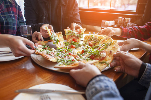 группа студентов друзья едят итальянскую пиццу, руки принимают ломтики пиццы в ресторане
 - Фото, изображение