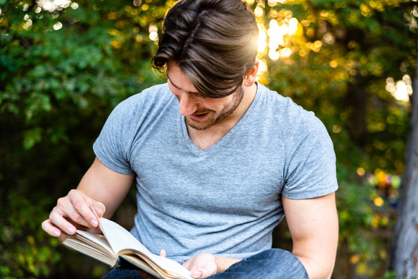 Een man leest een ontspannen roman zittend in een park bij zonsondergang, geliefde o - Foto, afbeelding