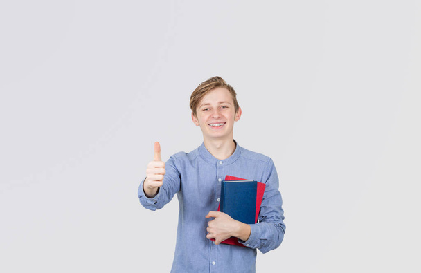 Gelukkige tiener jongen glimlachende duim omhoog gebaar met boeken. Boek - Foto, afbeelding