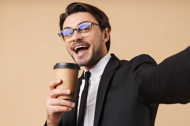 Εικόνα του χαρούμενου επιχειρηματία που κρατάει την κούπα του καφέ ενώ παίρνει selfi - Φωτογραφία, εικόνα