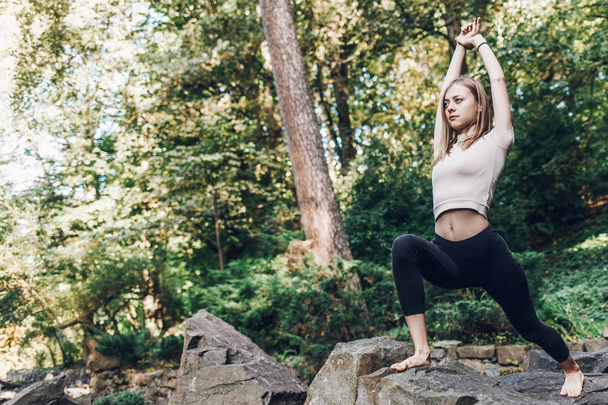 Chica joven profundiza el yoga mientras hace ejercicios en el parque en las rocas. Ejercicio de yoga al aire libre
 - Foto, imagen