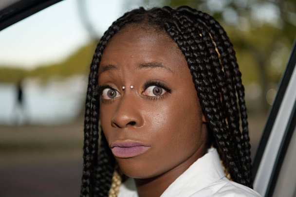 Close-up portret van een zwart Afro-stijl meisje verrast met lange zwarte vlechten in een auto - Foto, afbeelding