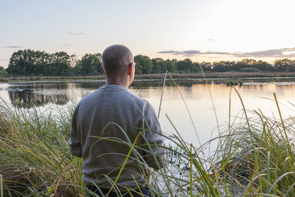 Un pescador atrapa peces en la orilla del estanque al amanecer
. - Foto, Imagen