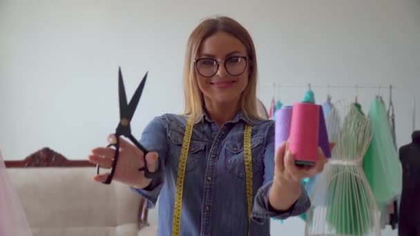Piękna szwaczka blondynka w studio szycia trzyma nożyczki i sznurki nici - Materiał filmowy, wideo