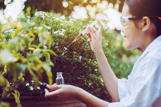 Asian woman researcher using syringe for examining and study information data in the garden - Photo, Image