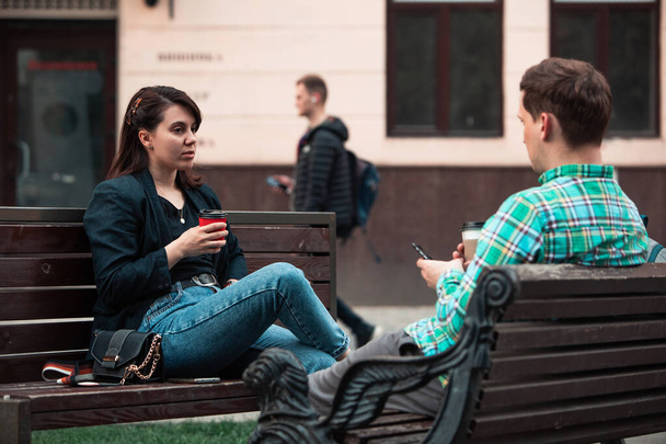 χαμογελαστός ζευγάρι που κάθεται στο παγκάκι και μιλάει ο ένας στον άλλο πίνοντας καφέ - Φωτογραφία, εικόνα