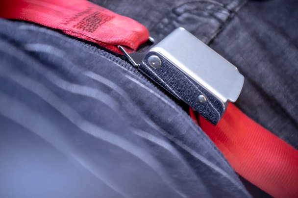 Man is fastened with a seat belt, red with a metal buckle, in an airplane. Safe flight concept. - Фото, изображение