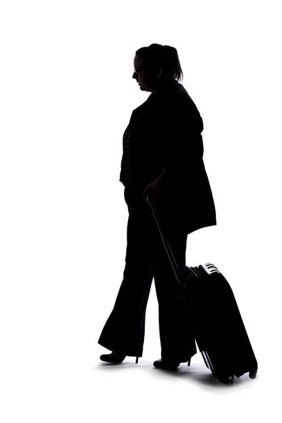 Silhouet van een zakenvrouw die op zakenreis gaat en met bagage reist. Ze draagt tassen als voorbereiding op een vlucht op een luchthaven..  - Foto, afbeelding
