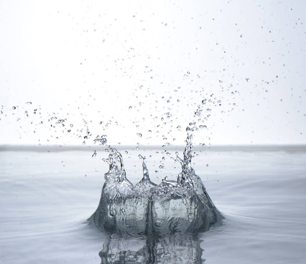Bewegend water op witte achtergrond, stralen en druppels - Foto, afbeelding