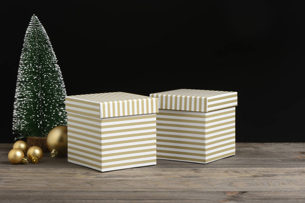 Gouden en witte gestreepte geschenkdozen op houten en zwarte ondergrond - Foto, afbeelding