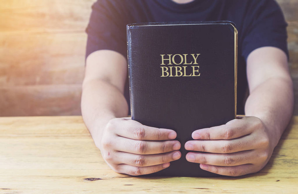 Close up of a man hand holding holy bible on  wooden table, Christian background with copy space - Foto, Bild